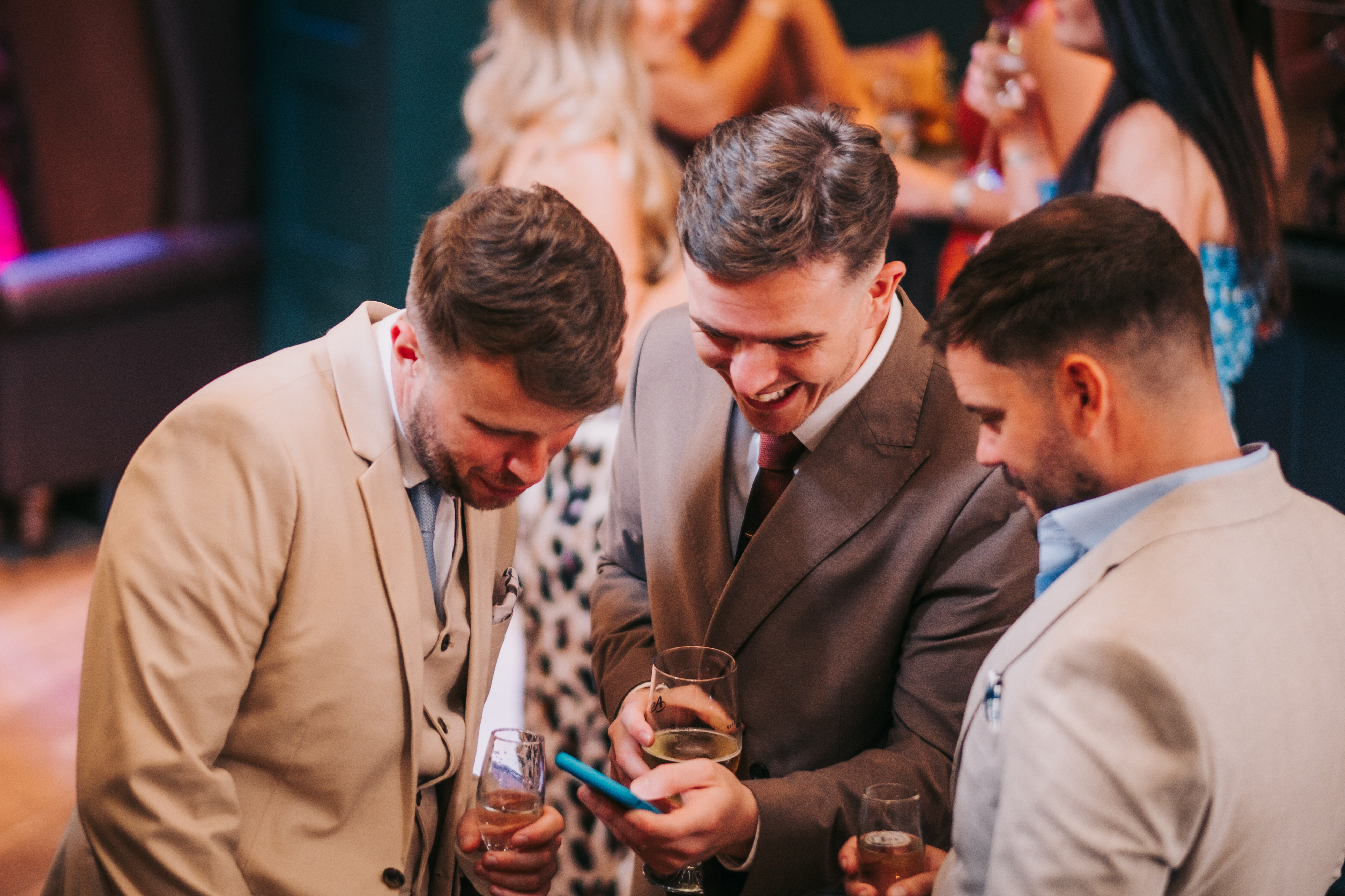Three male guests looking and laughing at something on a phone, drinks in hand. Three male guests looking and laughing at something on a phone, drinks in hand.