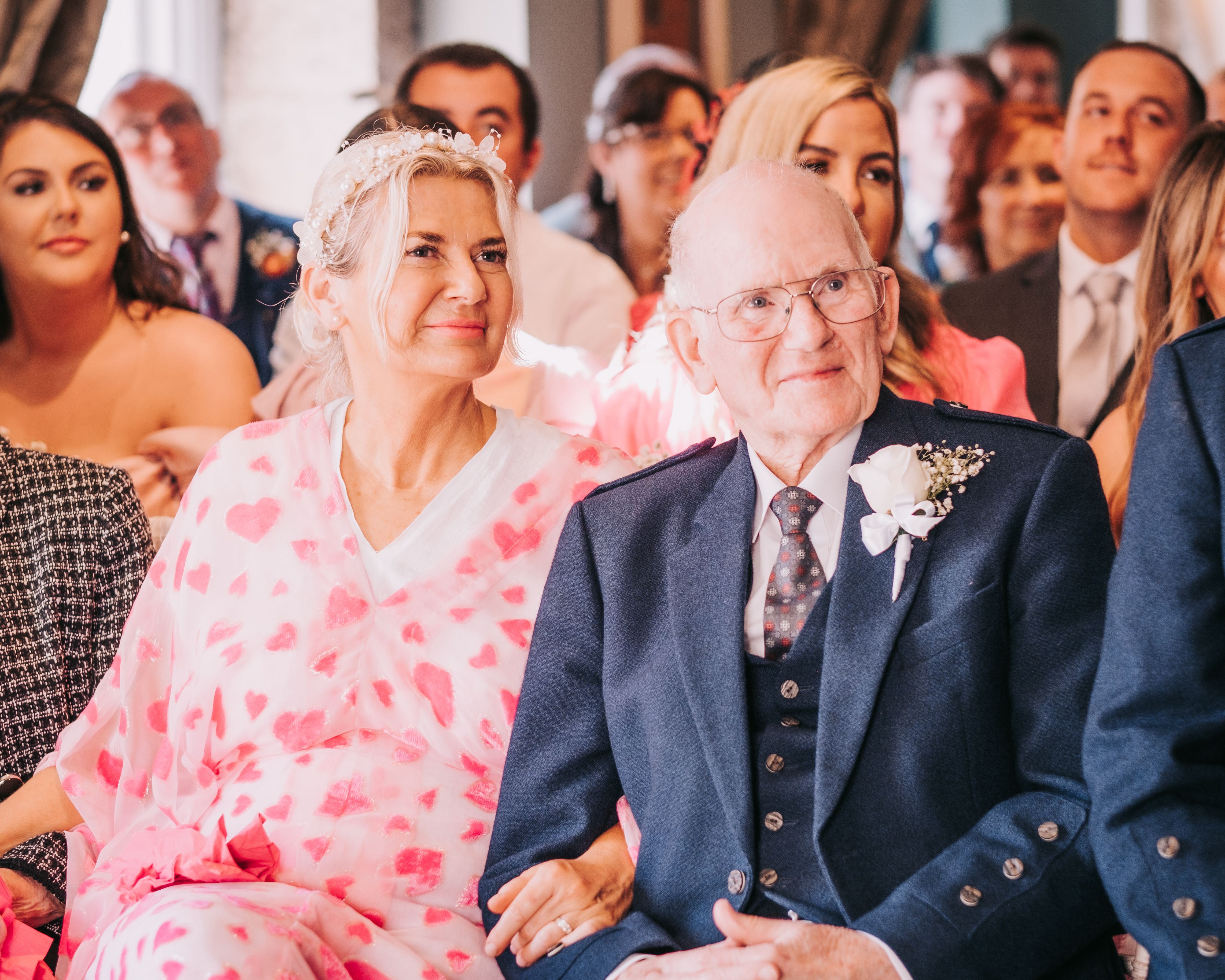 Mother of the Bride and grand-dad seated during ceremony, dressed formally with flower details Mother of the Bride and grand-dad seated during ceremony, dressed formally with flower details