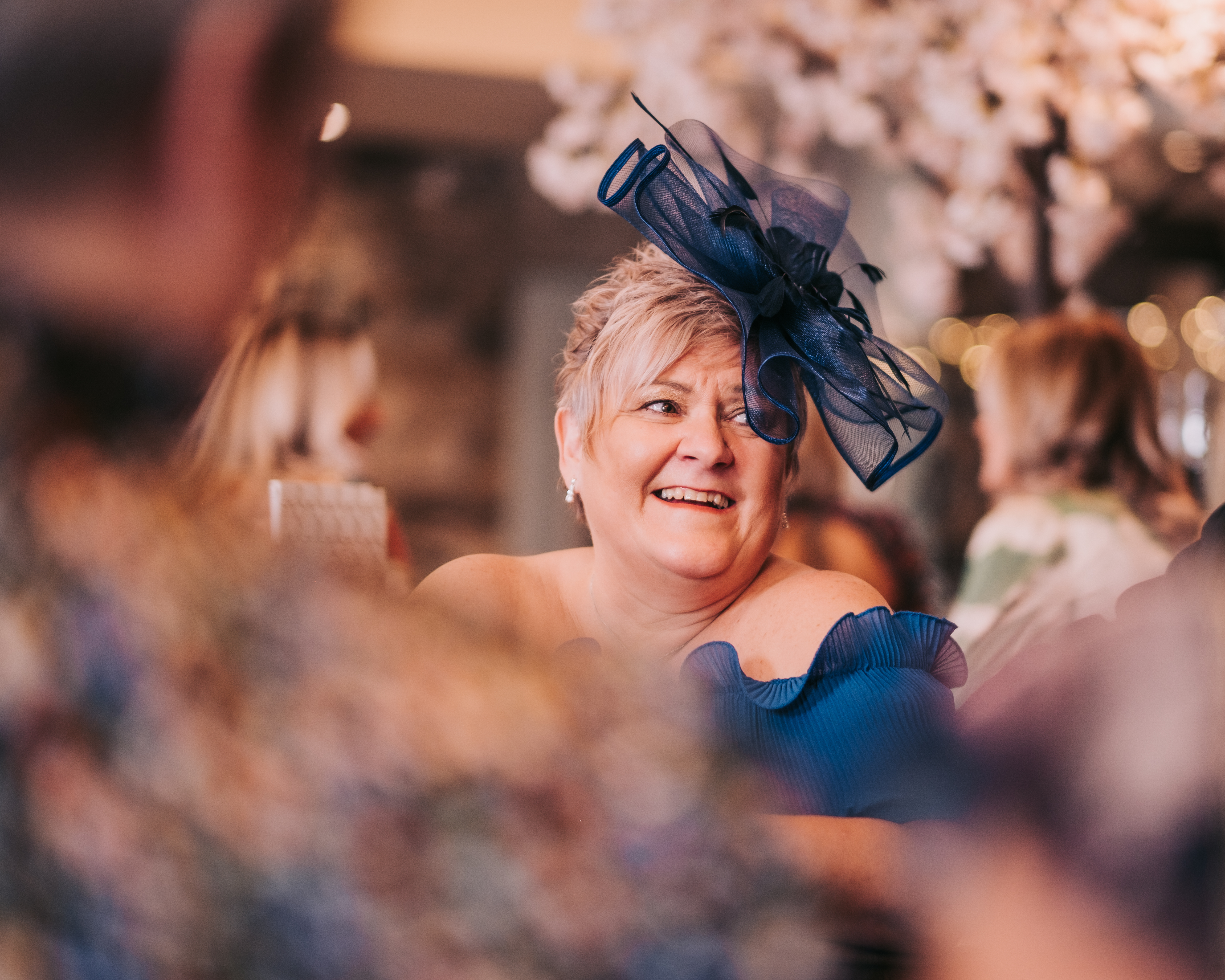 Female guest in bright blue dress and fascinator smiling warmly during the reception. Female guest in bright blue dress and fascinator smiling warmly during the reception.