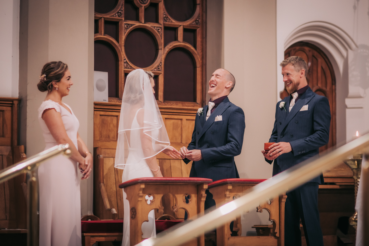 Image of couple exchanging rings at Holy Cross Church, laughing at an inside joke. Image of couple exchanging rings at Holy Cross Church, laughing at an inside joke.