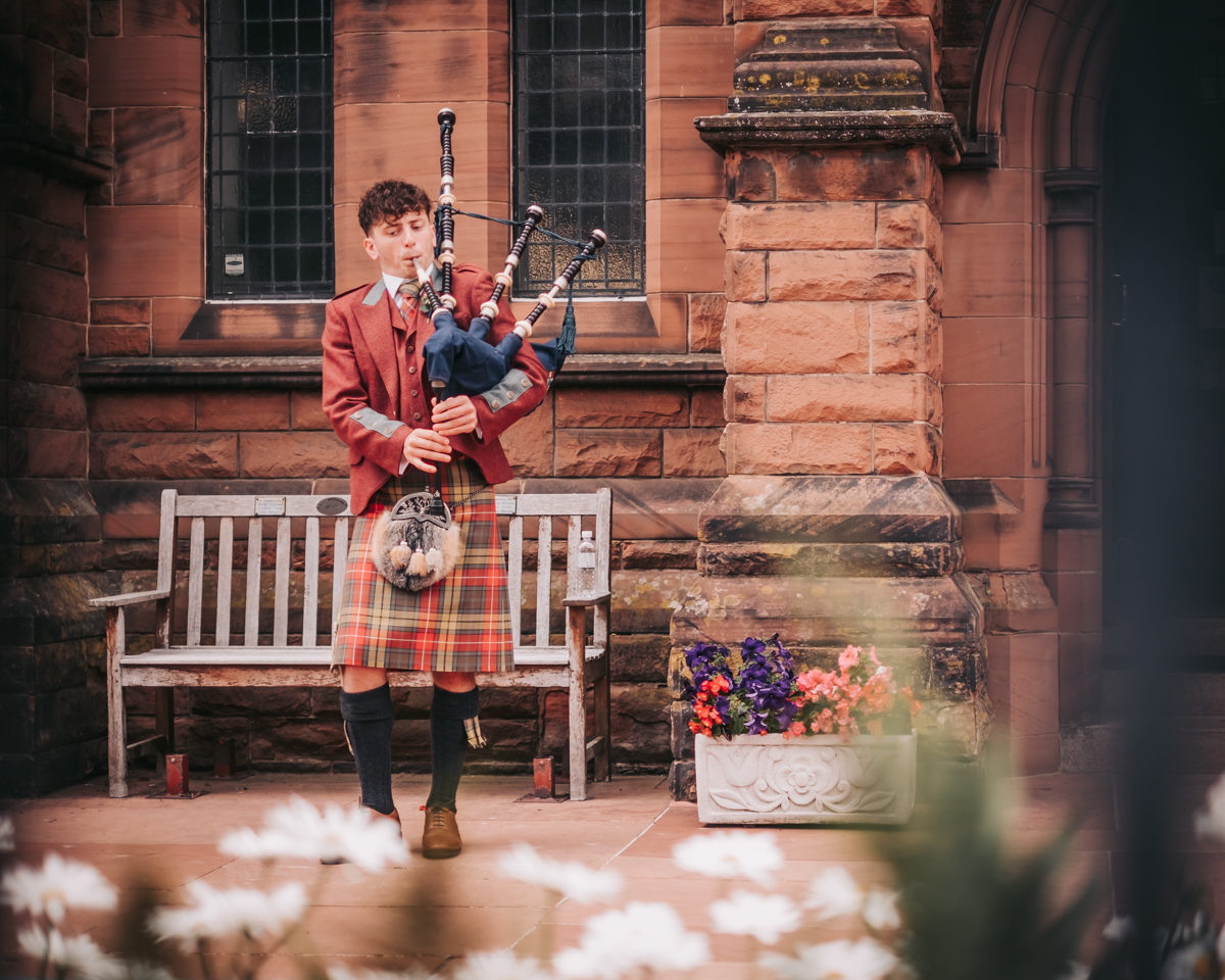 Wedding guest in a traditional Scottish kilt playing the bagpipes outside Holy Cross Catholic Church in Glasgow, marking the end of the ceremony with a celebratory tune. Wedding guest in a traditional Scottish kilt playing the bagpipes outside Holy Cross Catholic Church in Glasgow, marking the end of the ceremony with a celebratory tune.