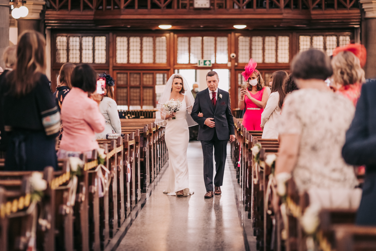 Bride and father of the bride walking down the aisle together, guests turning to smile and applaud. Bride and father of the bride walking down the aisle together, guests turning to smile and applaud.
