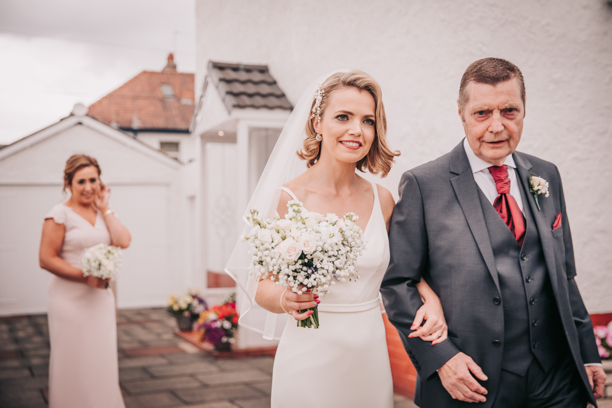Bride holding her bouquet in one hand, the her dad's hand in the other, as they make their way to the wedding car. Bride holding her bouquet in one hand, the her dad's hand in the other, as they make their way to the wedding car.