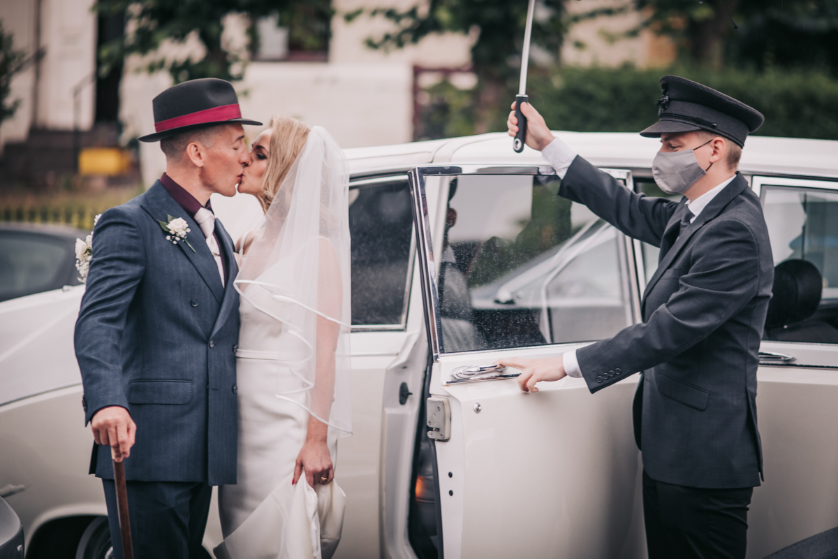 Groom and bride kissing beside the wedding car as they prepare to leave ceremony to travel to reception venue. Groom and bride kissing beside the wedding car as they prepare to leave ceremony to travel to reception venue.