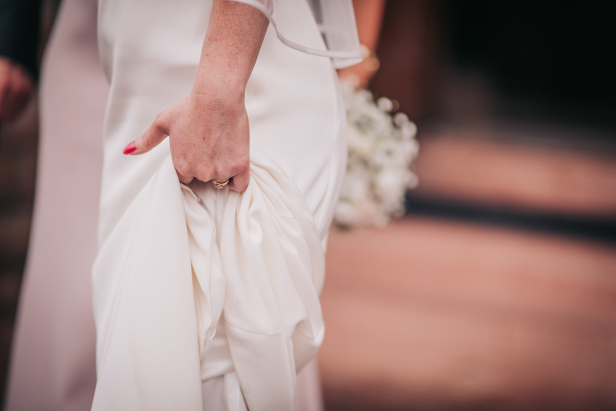 Bride clutches her Sassi Holford wedding gown outside Holy Cross Church, Glasgow Bride clutches her Sassi Holford wedding gown outside Holy Cross Church, Glasgow