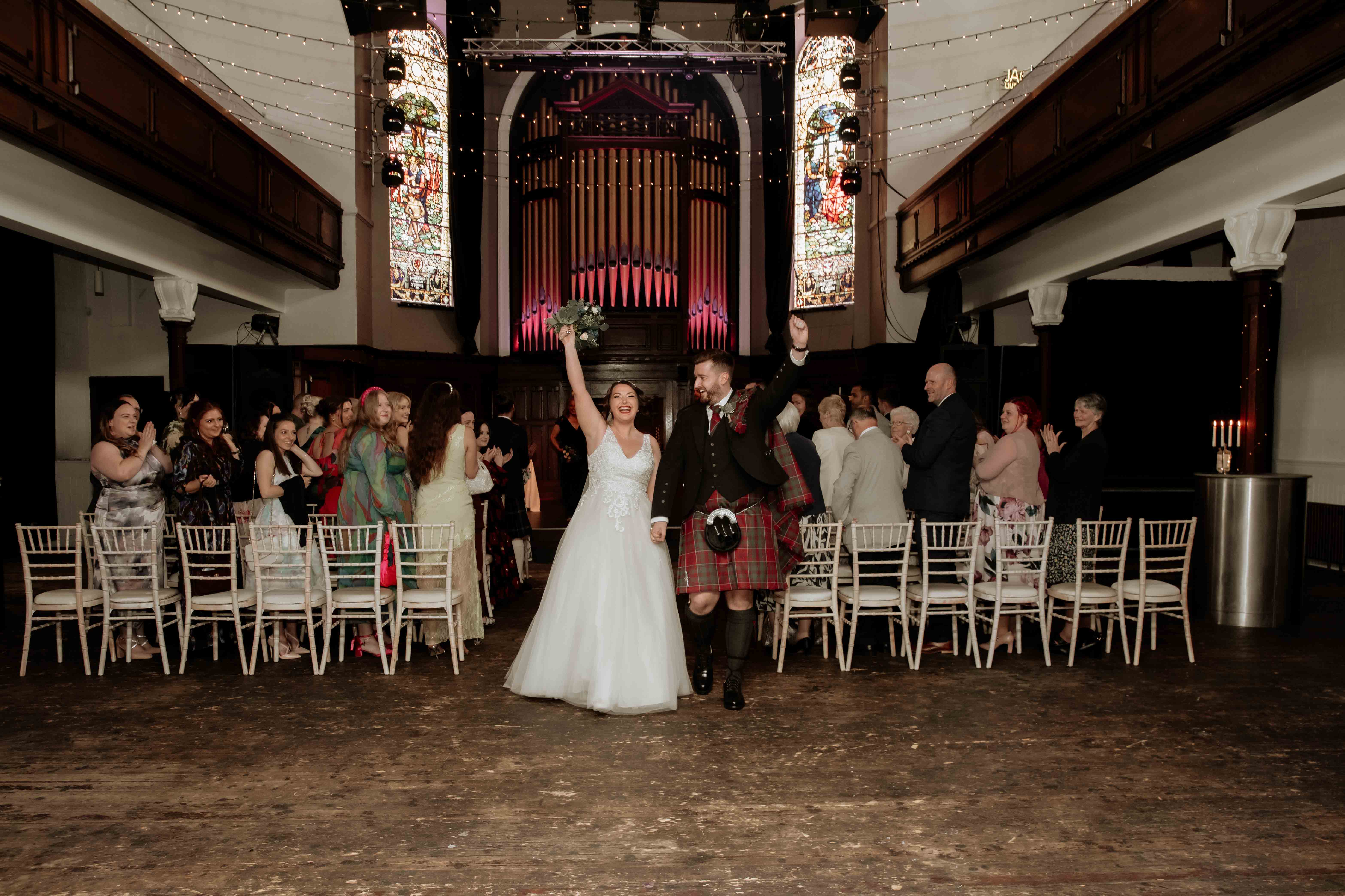 Bride and groom celebrating their newly made vows as they walk down the aisle and out of the ceremony room, St. Luke's, Glasgow. Bride and groom celebrating their newly made vows as they walk down the aisle and out of the ceremony room, St. Luke's, Glasgow.
