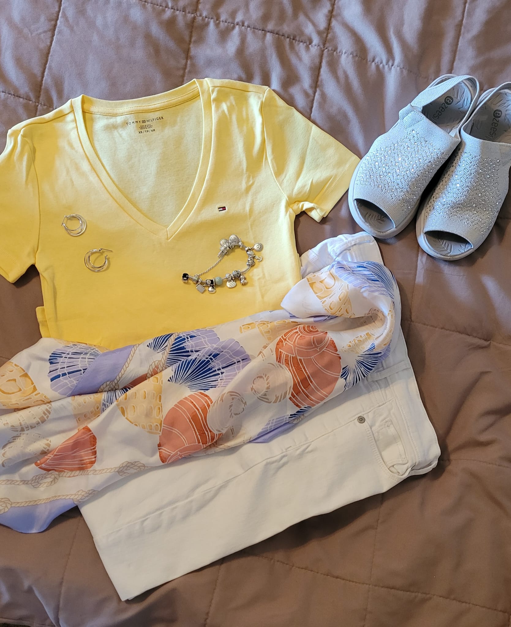 Flat lay outfit featuring a yellow Tommy Hilfiger v-neck tee, LOFT white jeans, a LOFT shell-print scarf worn as a belt or neck accessory, sparkly white Bzees sandals, silver earrings, and a Pandora bracelet — styled by Jenn.