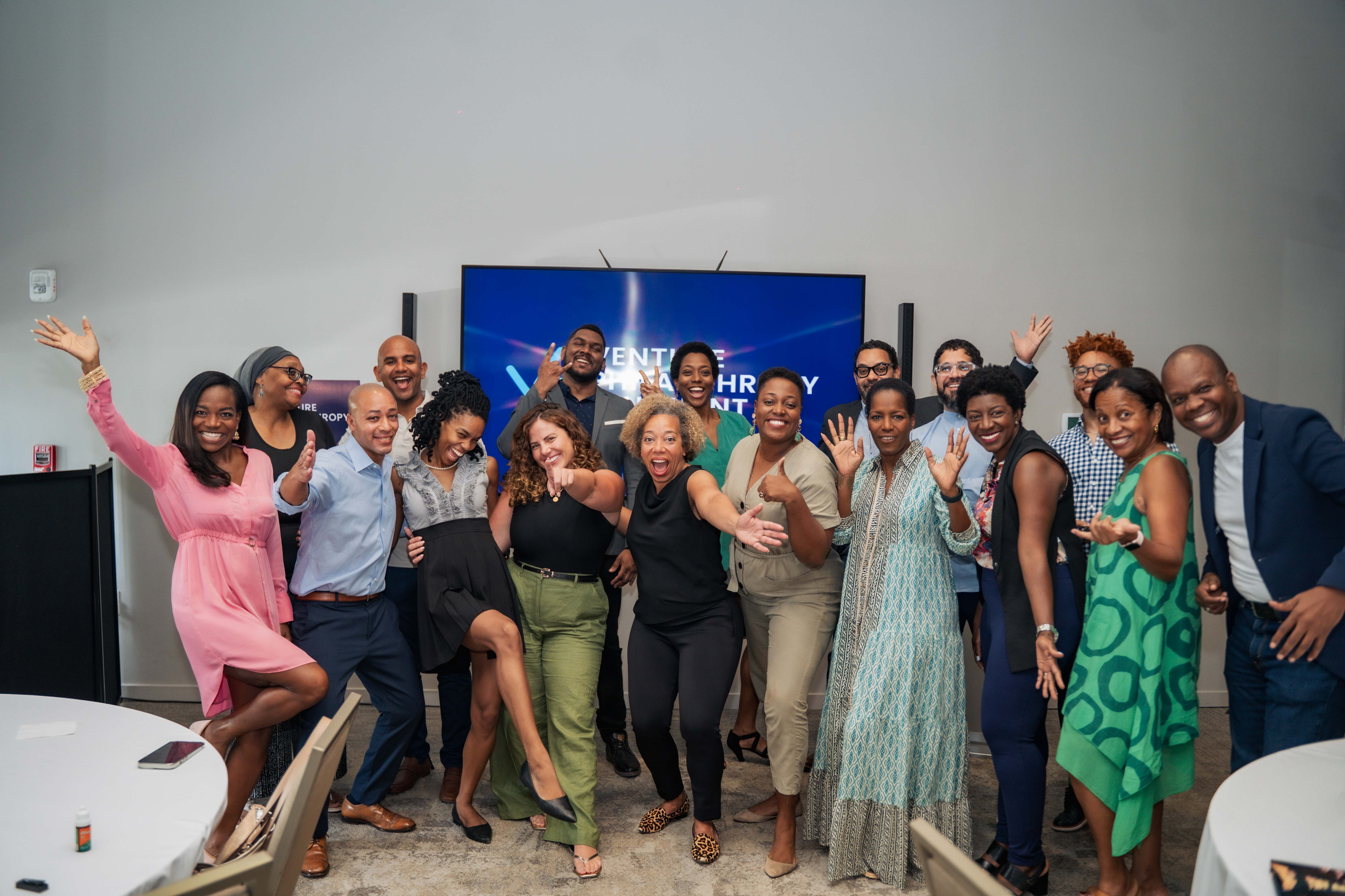 A vibrant group of attendees poses enthusiastically for a group photo at the Venture Philanthropy Blueprint Power Brunch event in Kingston, Jamaica. Standing in front of a large screen with the VPB logo, the diverse group of changemakers, entrepreneurs, and impact leaders celebrates with joyful expressions and animated gestures, reflecting the energy and spirit of the event.