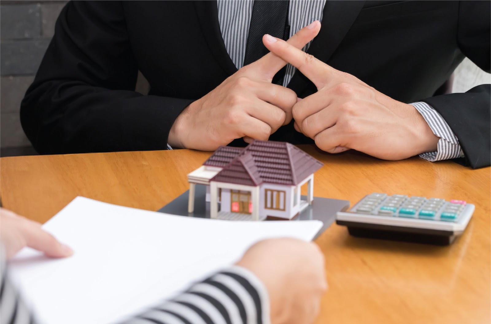 A real estate agent crosses his fingers with a house model and calculator, symbolizing securing No bank financing homes with KBR Investing. A real estate agent crosses his fingers with a house model and calculator, symbolizing securing No bank financing homes with KBR Investing.