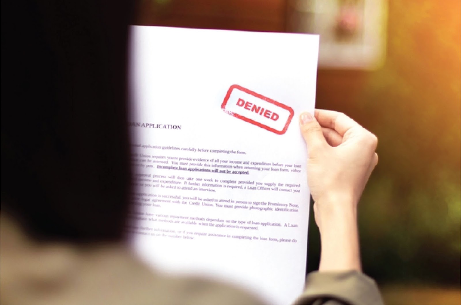 A person holds a loan application form with a "DENIED" stamp, showing KBR Investing offers Non-bank home financing. A person holds a loan application form with a "DENIED" stamp, showing KBR Investing offers Non-bank home financing.