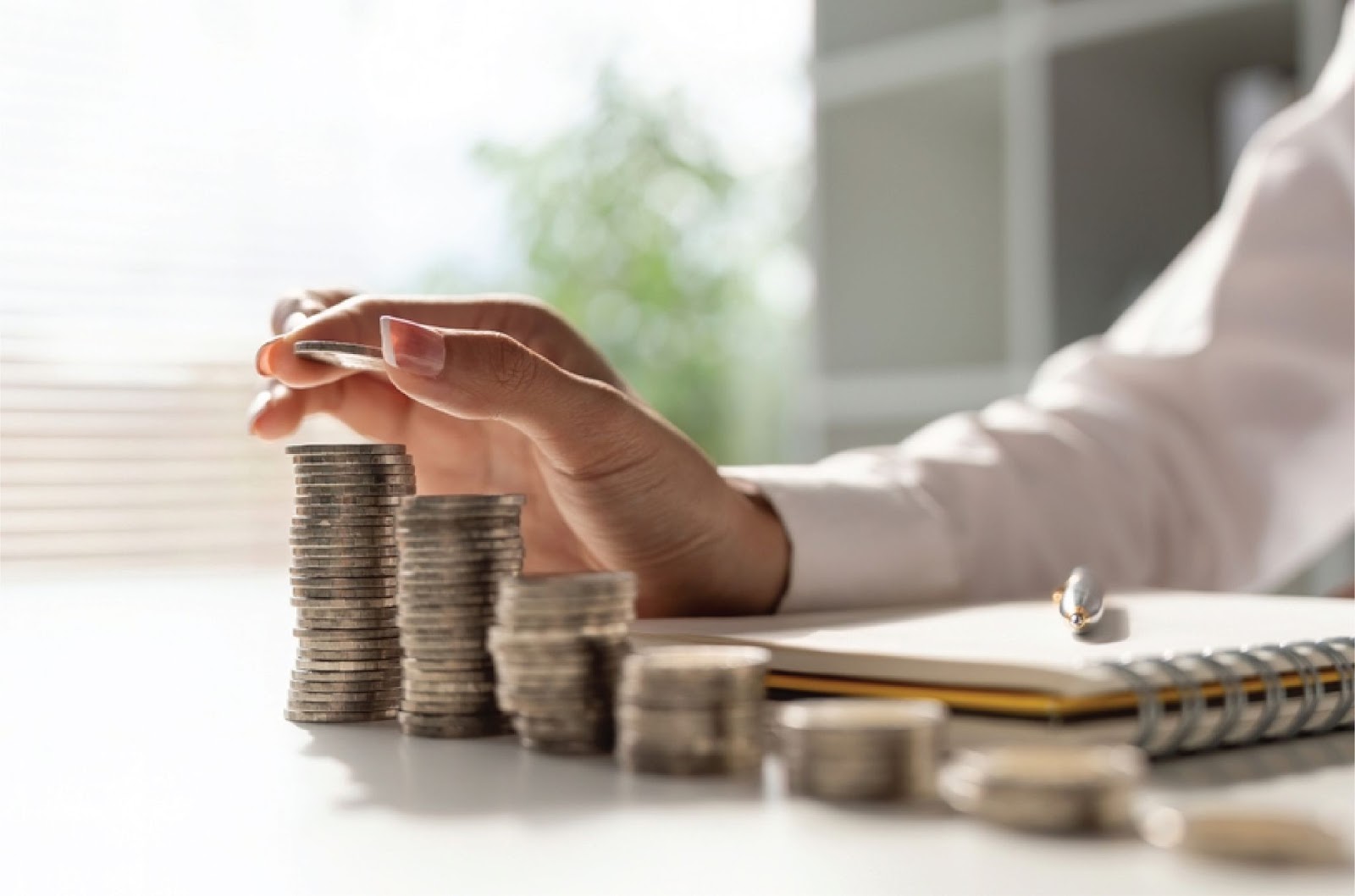 A hand stacks coins beside a notebook, showing how to Qualify for owner financing with KBR Investing A hand stacks coins beside a notebook, showing how to Qualify for owner financing with KBR Investing