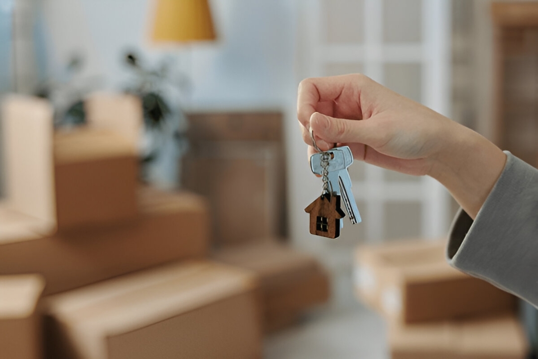  A hand holds house keys and a house keychain, representing Kbr investing's assistance with Qualifying for owner financing loans.