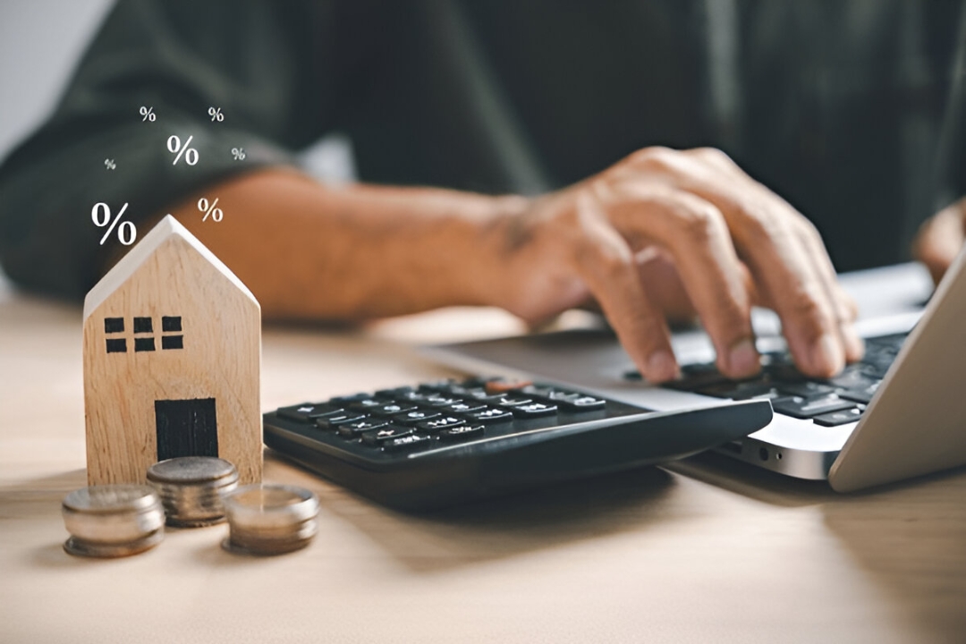  An individual calculates finances at a desk, with a house model and coins, showcasing Kbr investing's solutions for Owner financing after bank rejection.