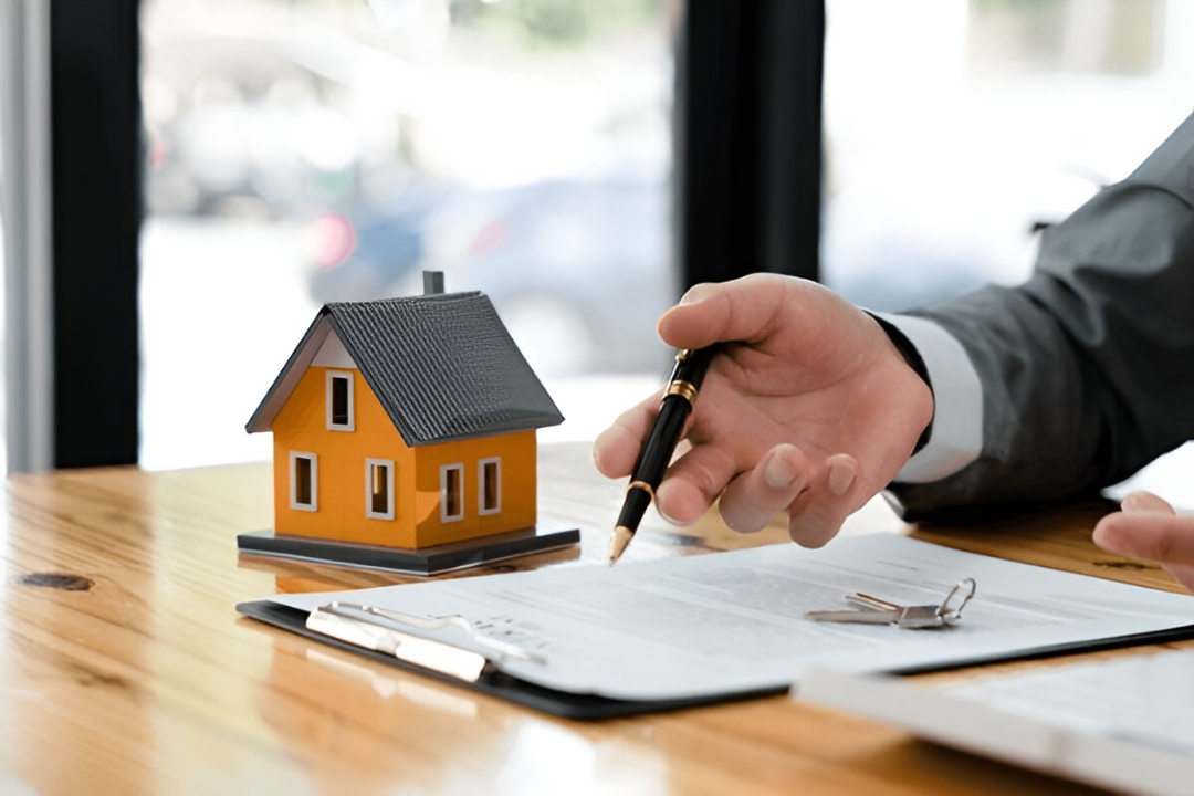 A person signs a contract next to a model house and keys, representing Kbr investing's guidance to Buy a home without a loan.