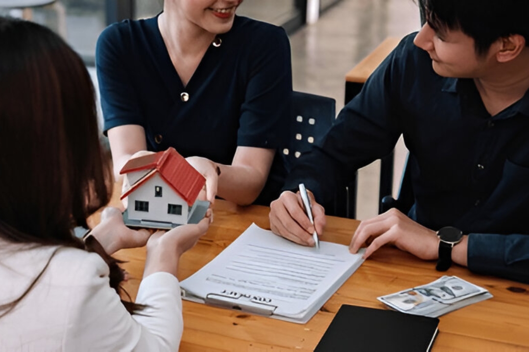 A couple signs documents with a real estate agent and a model house, symbolizing a way to Buy a house without mortgage with Kbr investing.