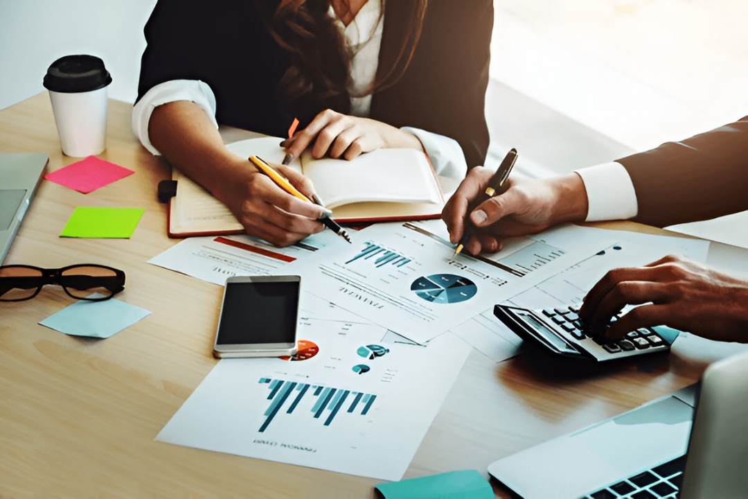 Two professionals review financial charts and use a calculator, representing guidance from KBR Investing to Buy a house with low credit in the U.S.