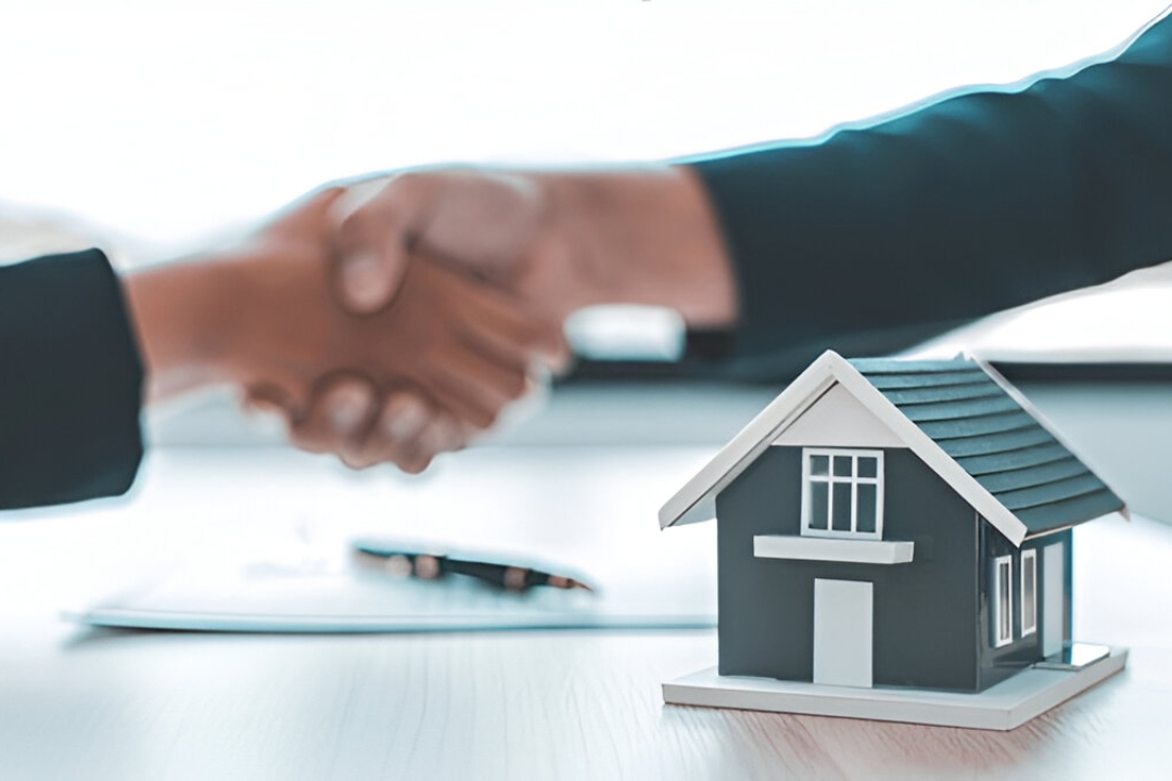 Two people shake hands over a desk with a model house, symbolizing a successful agreement for flexible down payment options for homes with KBR Investing.