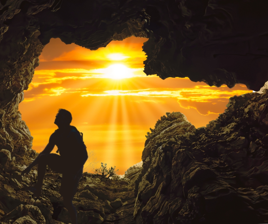 Man climbing out of a rocky pit toward golden sunlight and hope