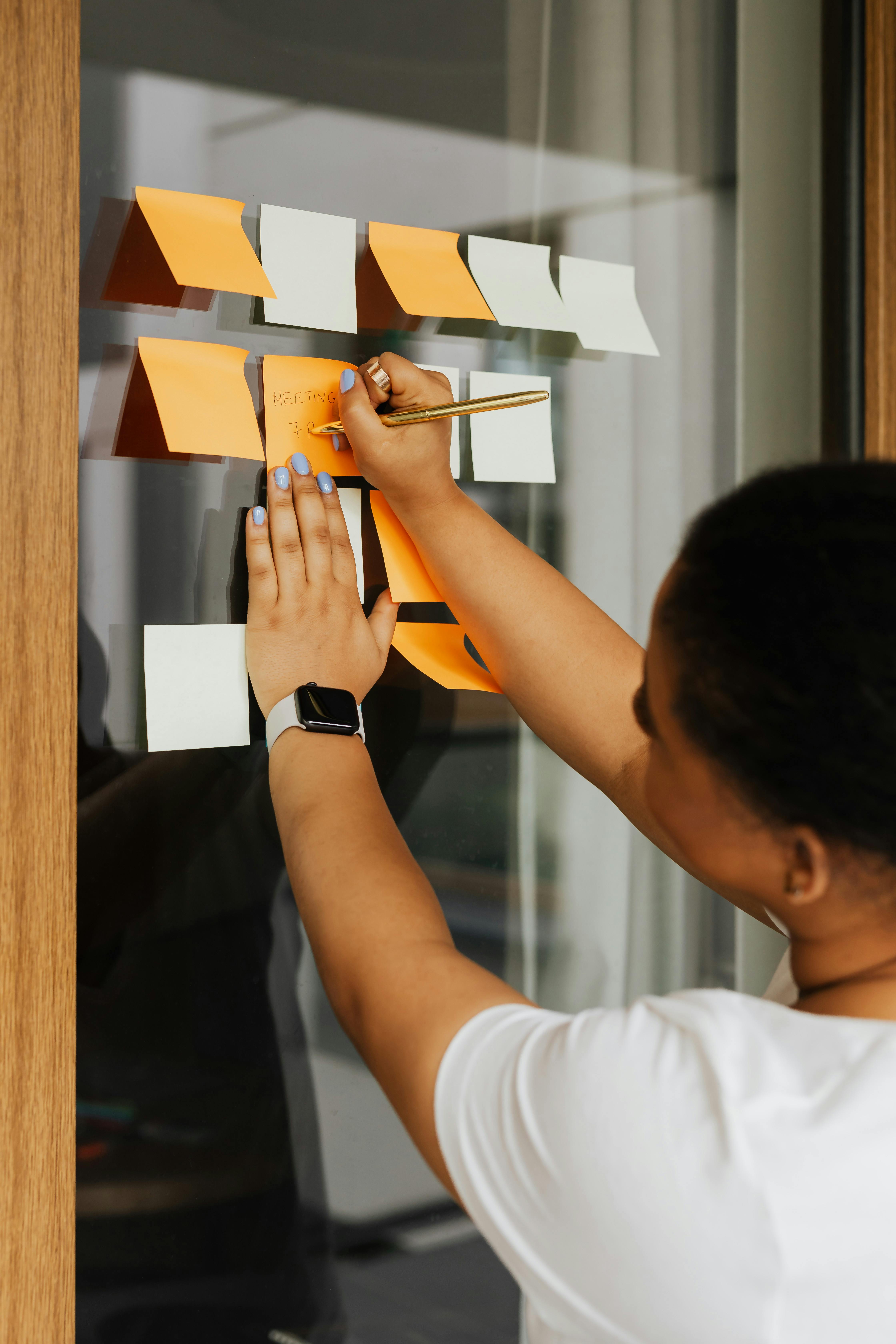 young woman writing on sticky notes attached to a wall young woman writing on sticky notes attached to a wall