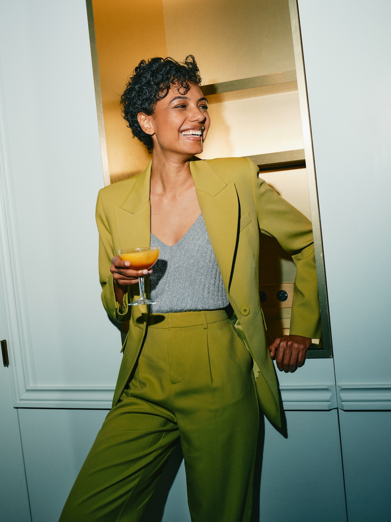 black woman in a green suit leaning against a counter with a cocktail in her hand black woman in a green suit leaning against a counter with a cocktail in her hand