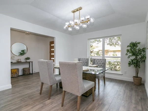 A stylish dining room undergoing remodeling with a modern chandelier, glass dining table, and large windows.