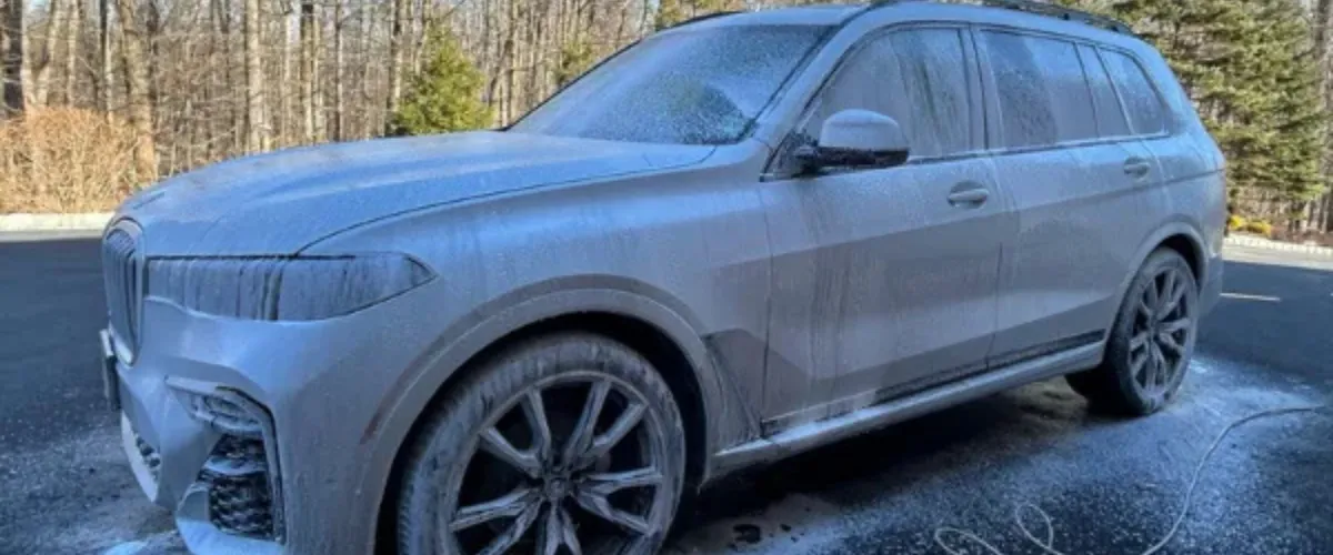 A BMW SUV covered in thick foam during an exterior car wash for deep cleaning.
