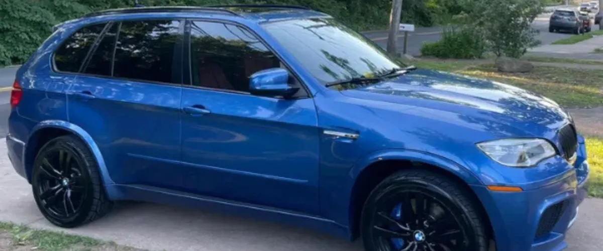 Side profile of a blue BMW X5M with black rims parked on driveway.