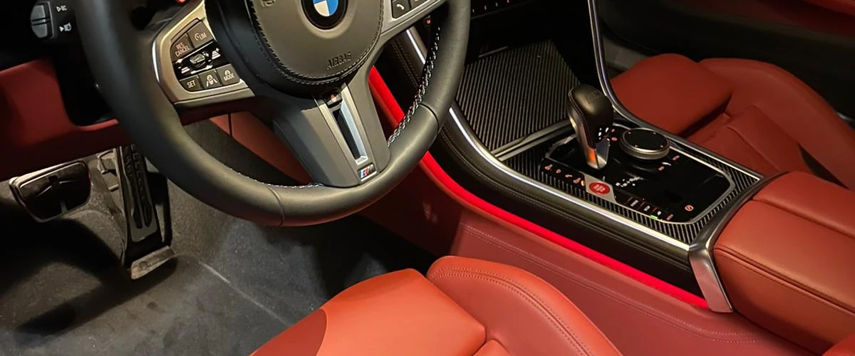 “BMW interior showing detailed steering wheel, console, and red leather seats.