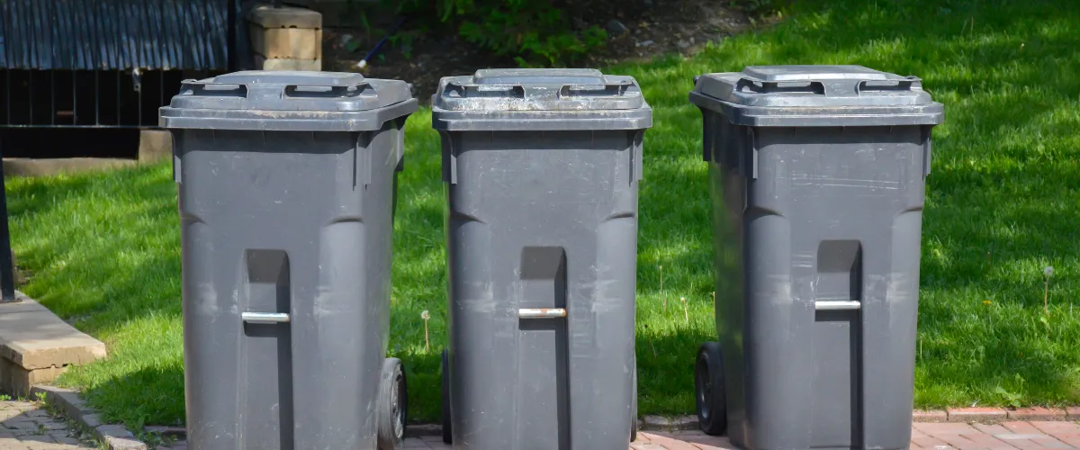 Three gray trash bins lined up on a clean brick pathway Three gray trash bins lined up on a clean brick pathway