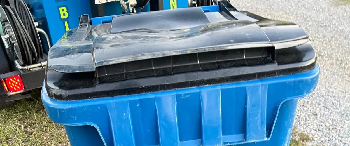 Close-up of a blue trash bin showing a warped and damaged black plastic lid
