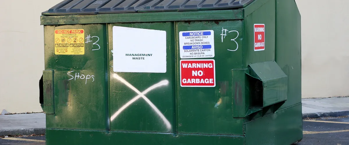 Green dumpster marked for cardboard only, covered in warning and restriction labels