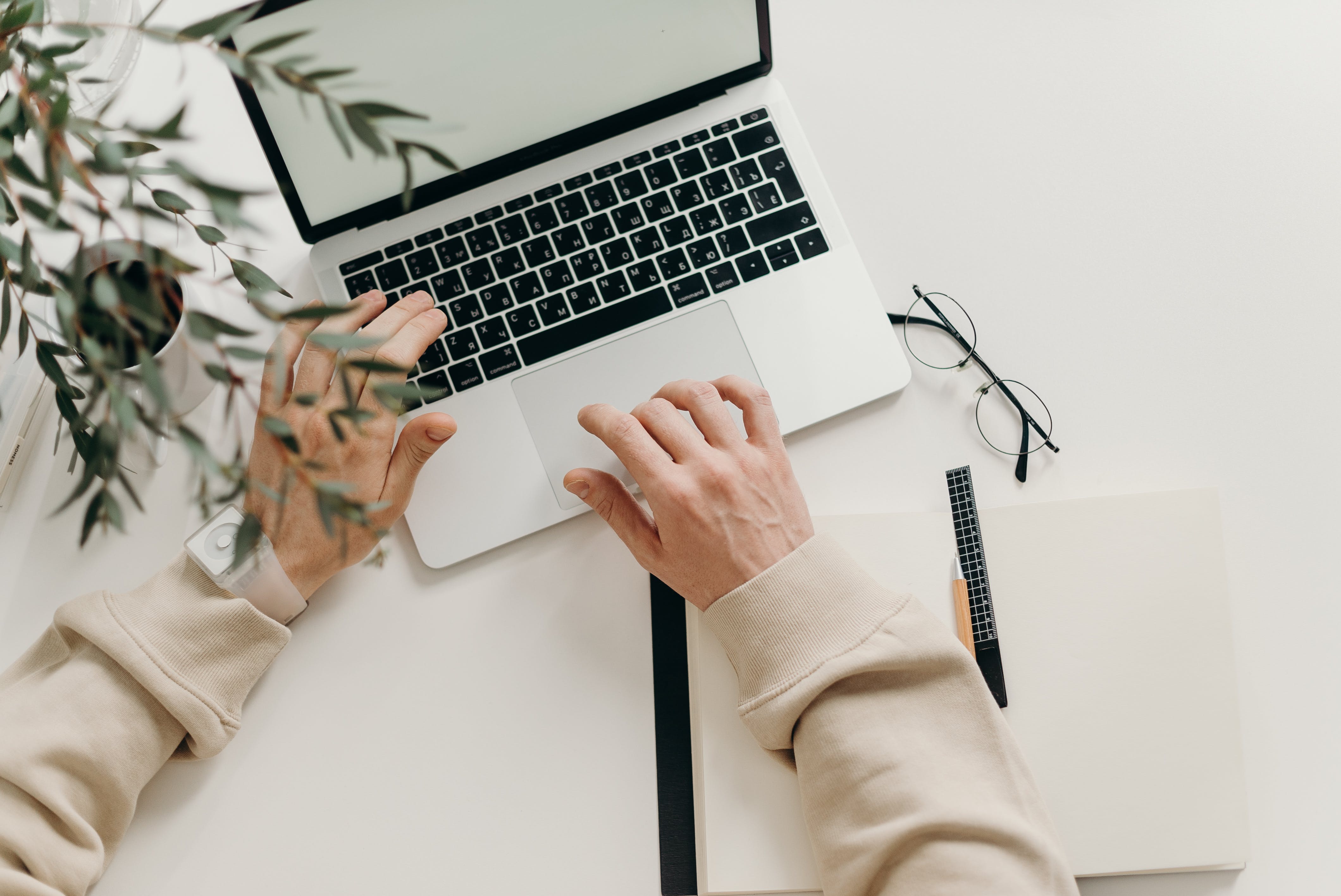 person with a beige shirt has hands over the keyboard of a laptop