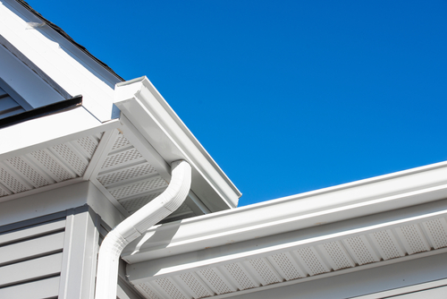 Close-up of a white gutter system attached to a residential roofline with blue sky in the background, highlighting the importance of proper gutter installation for home protection. Close-up of a white gutter system attached to a residential roofline with blue sky in the background, highlighting the importance of proper gutter installation for home protection.