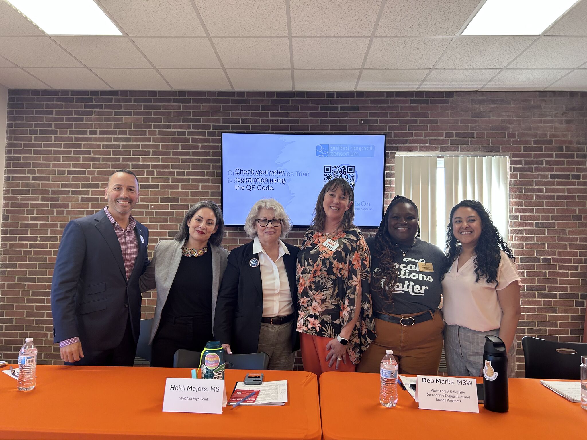 Group of nonprofit advocates standing up, arms around each other, posing for a picture behind a table. Group of nonprofit advocates standing up, arms around each other, posing for a picture behind a table.