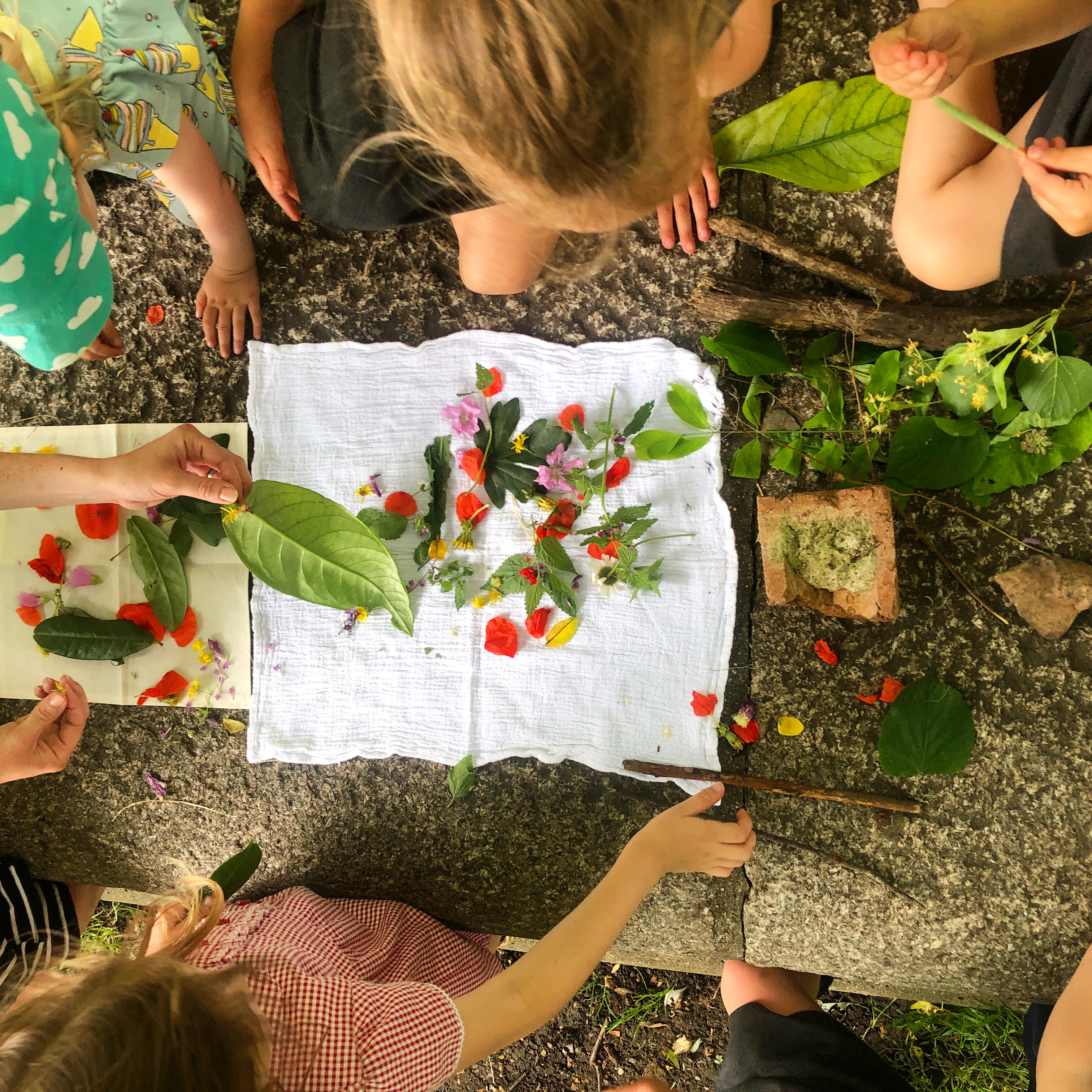 children surrounding a piece of fabric with flowers placed on top children surrounding a piece of fabric with flowers placed on top