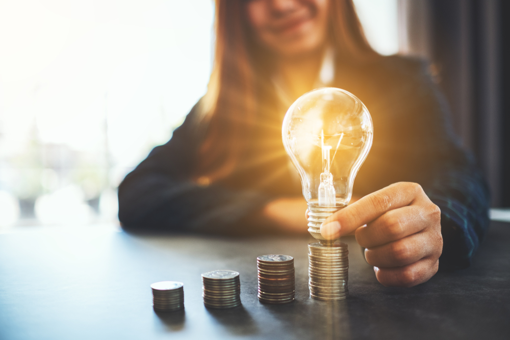 Businesswoman holding and putting lightbulb on coins stack on table for saving energy and money concep Businesswoman holding and putting lightbulb on coins stack on table for saving energy and money concep