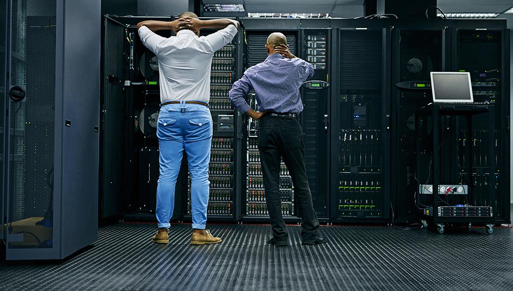 Two IT specialists stare at a server rack during a data loss crisis. Two IT specialists stare at a server rack during a data loss crisis.