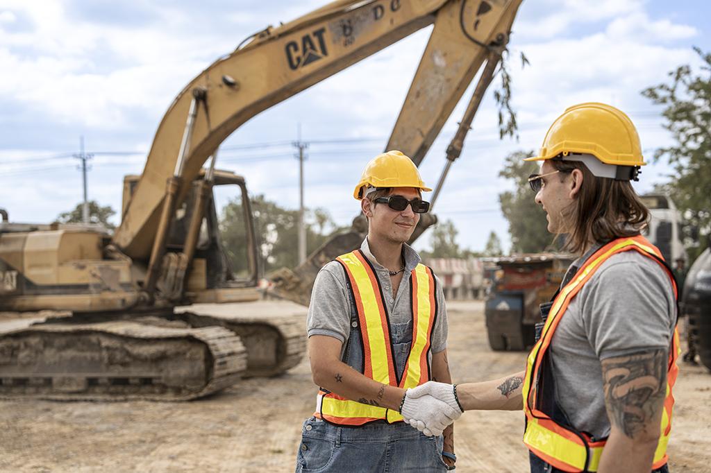 Construction company workers in hard hats and reflective vests shaking hands at a construction site Construction company workers in hard hats and reflective vests shaking hands at a construction site