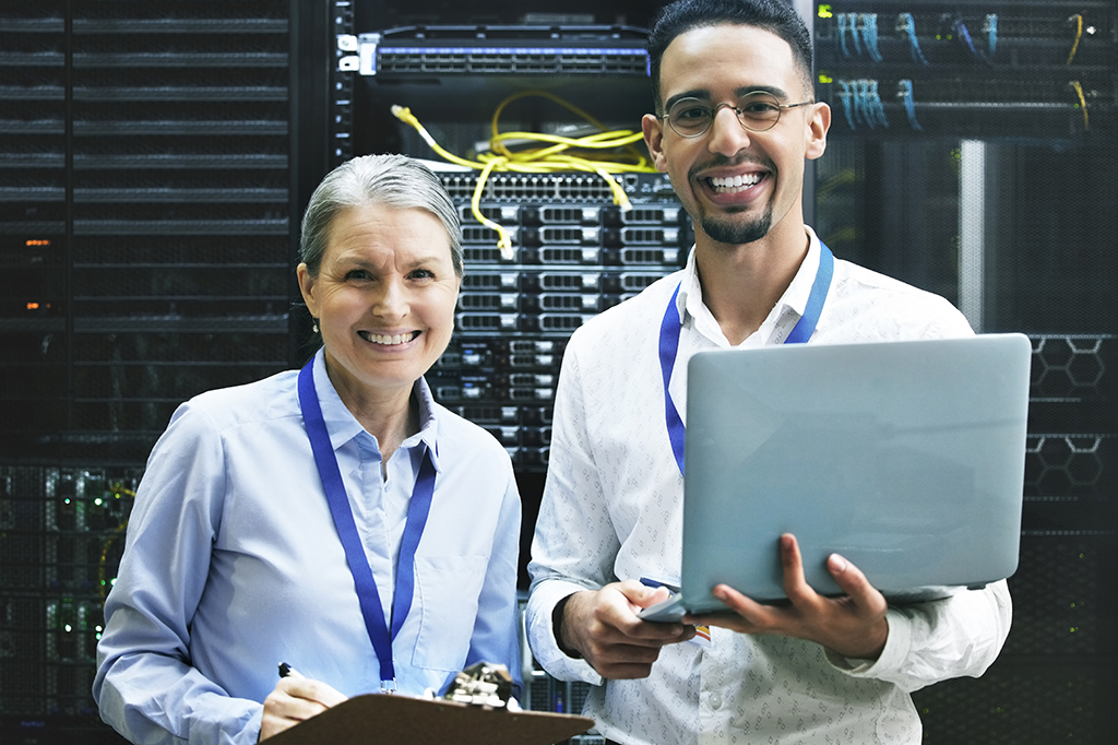 Two IT specialists in a server room stand smiling, ready to help.