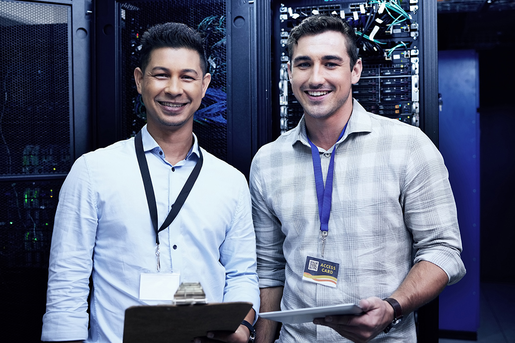 Smiling IT technicians standing in front of a server farm. Smiling IT technicians standing in front of a server farm.