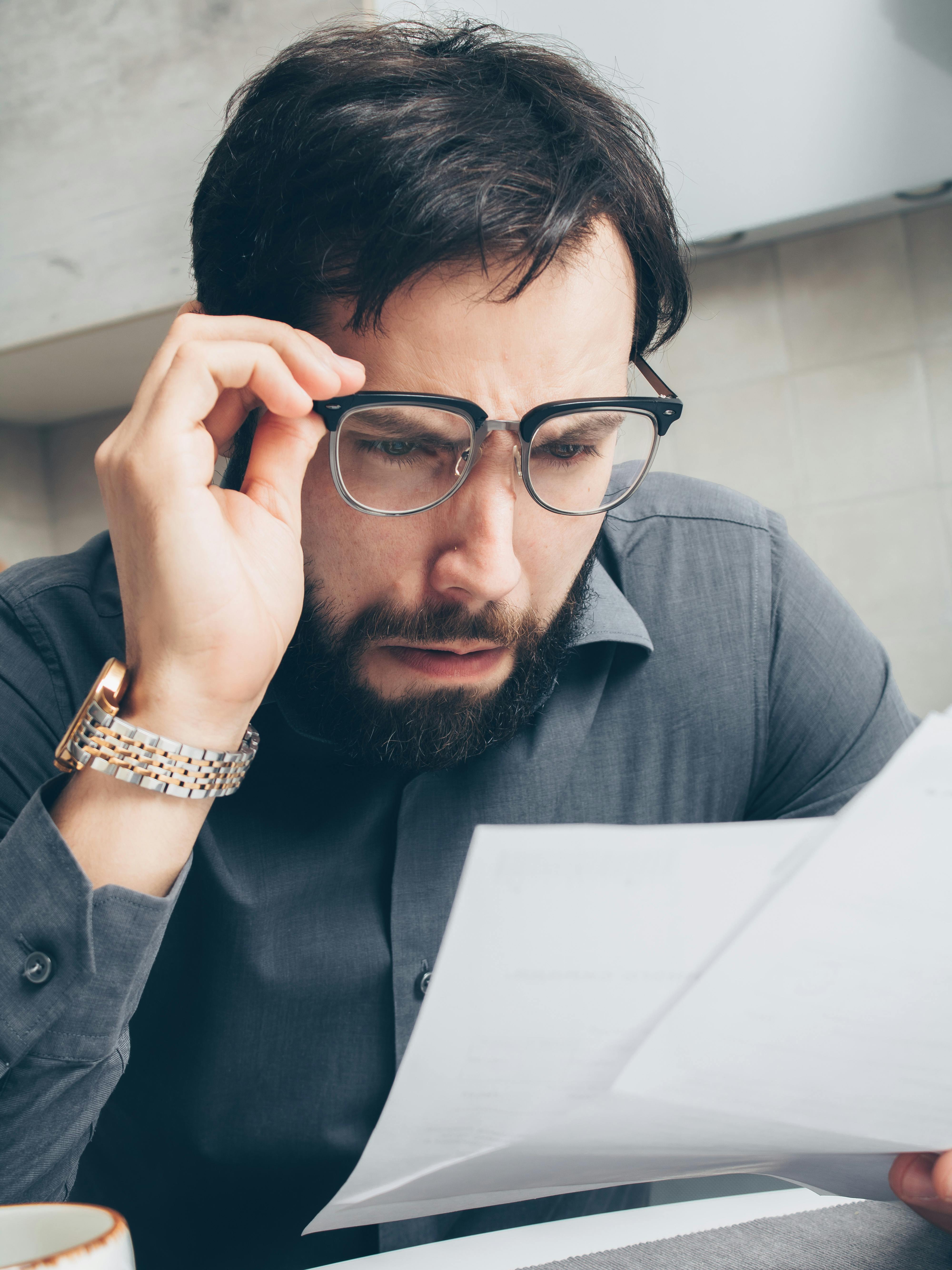 Stressed man with glasses over unpaid bills to support blog post Understanding ADHD Tax, Financial Costs & Tips to Avoid