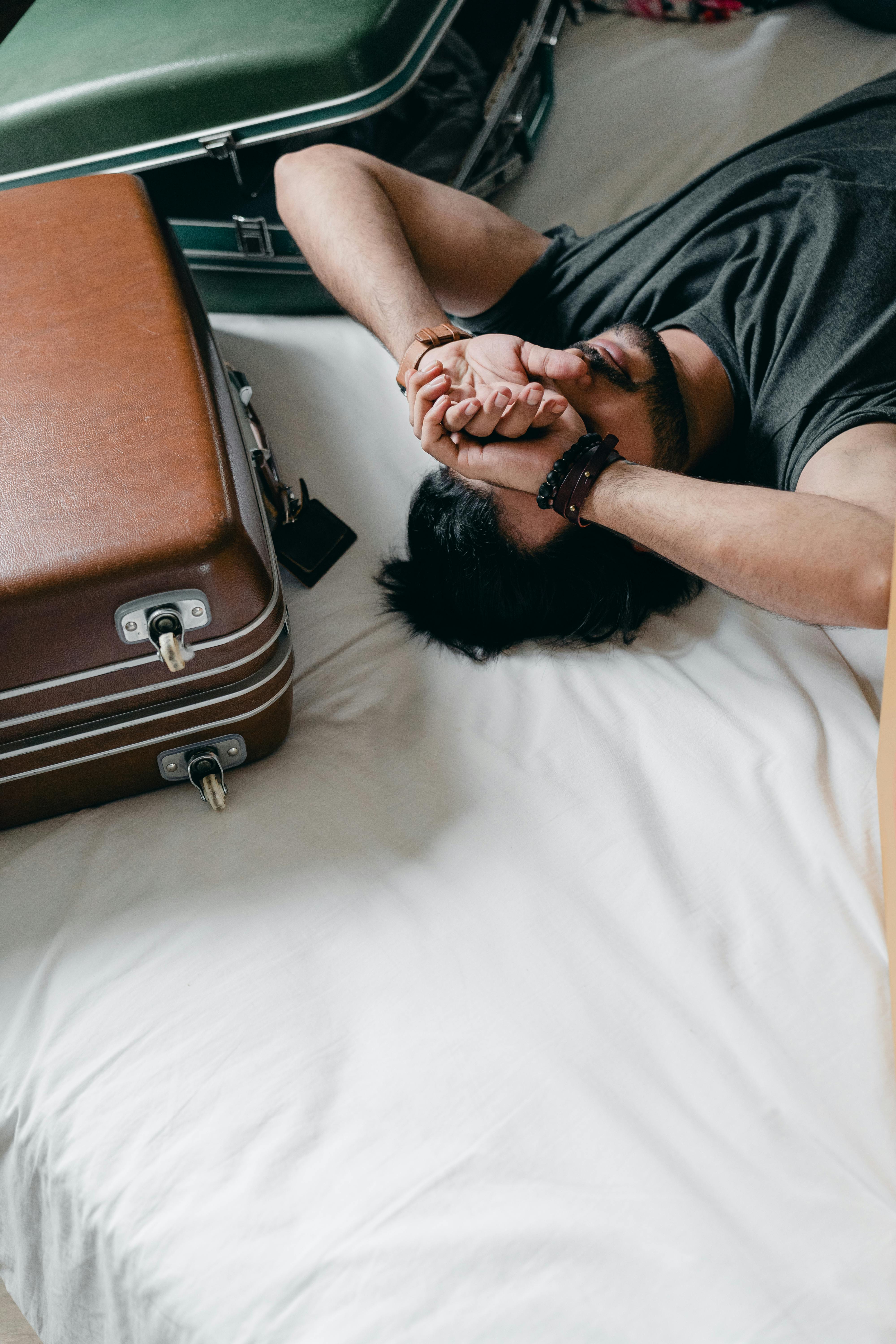 Many lying on bed surrounded by suitcases and overwhelmed to support blog post Is OCD Considered to be linked to Neurodivergence