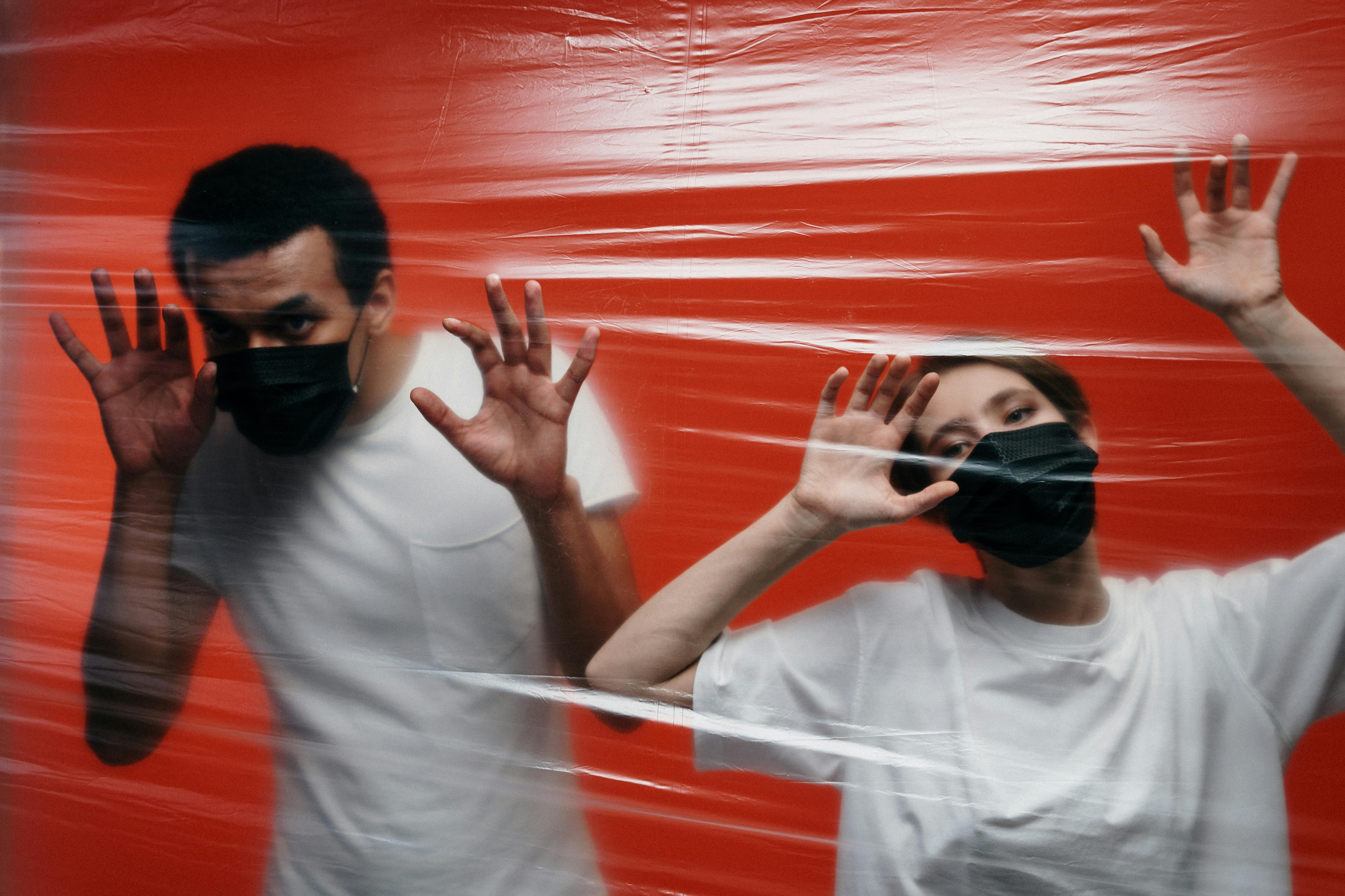 Two people with facemasks on pushing agains clingfilm that is a barrier to life to support blog post Is OCD Considered to be Linked to Neurodivergent People?