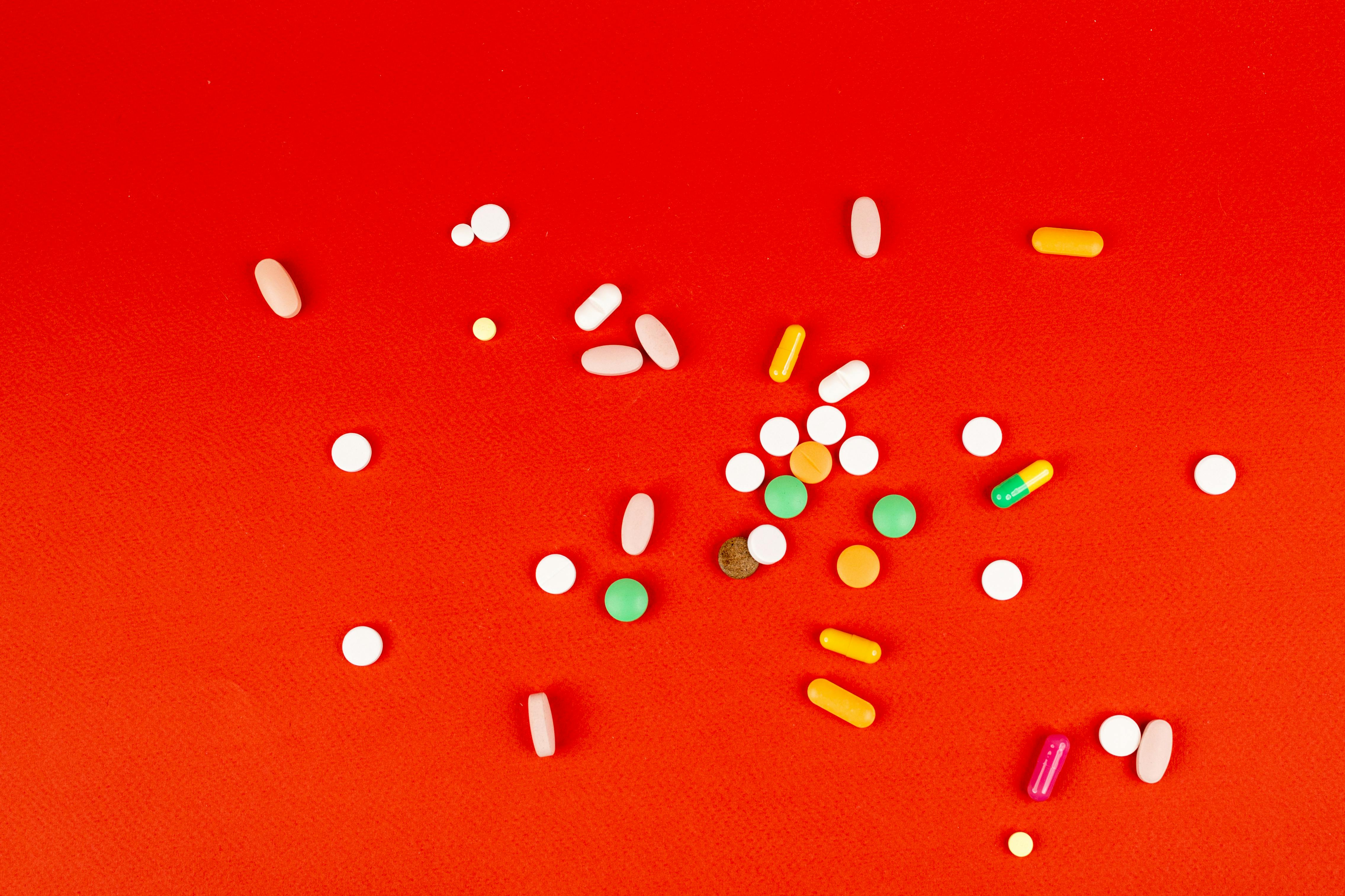 Selection of medical pills layed out on red background to support blog post ADHD Medications Guide: Dose, Switching, and Comparison