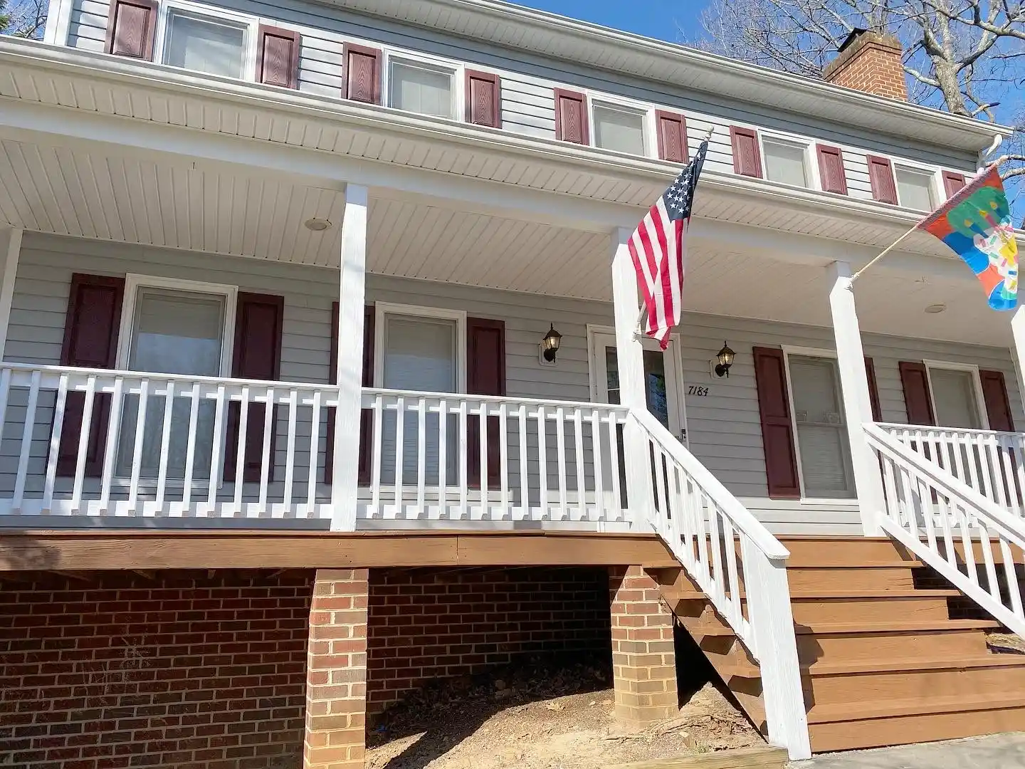 A charming house with a painting exterior, featuring a porch with white railings, an American flag, and a colorful decorative flag.