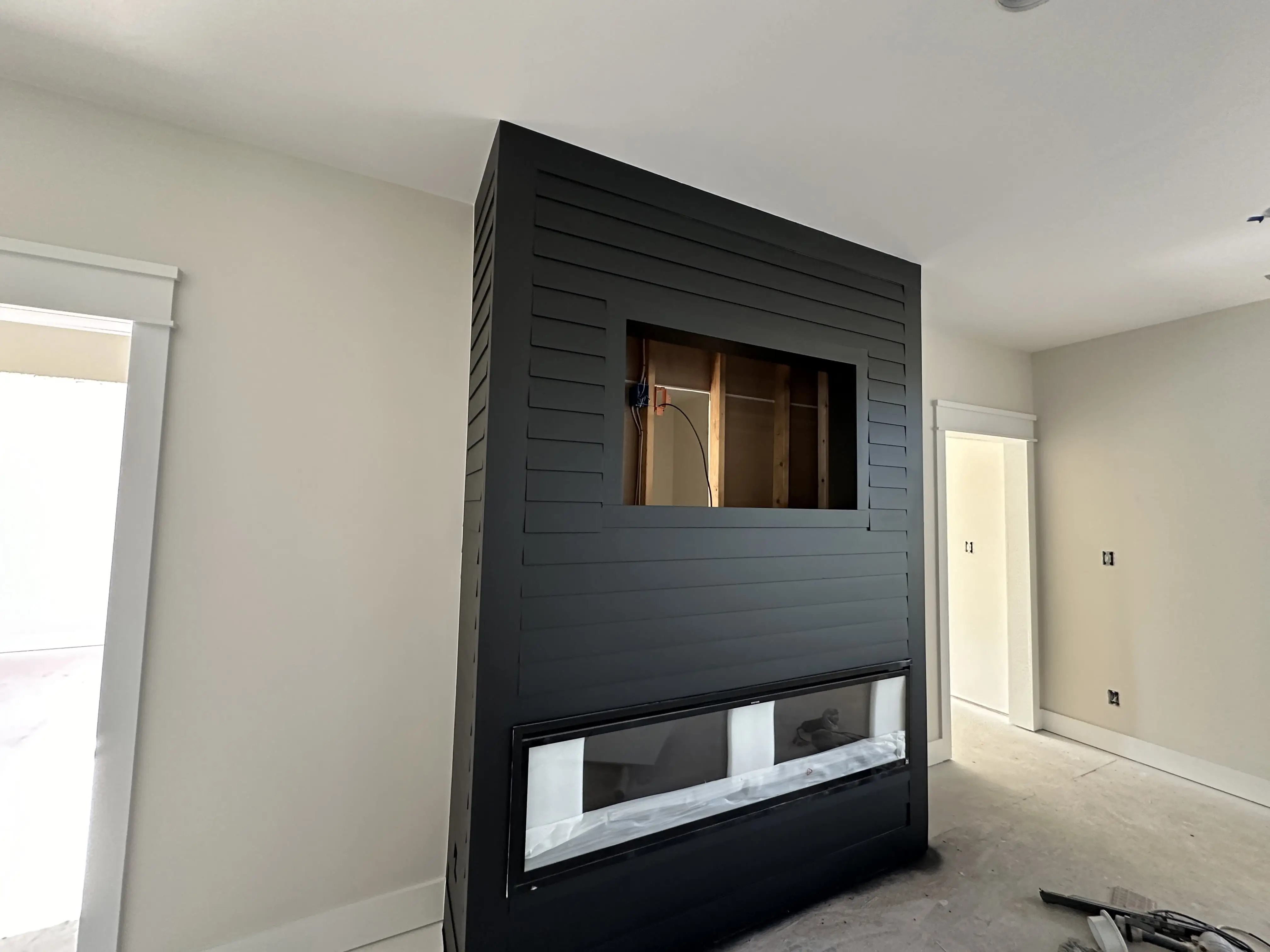 A modern room with a painting black fireplace under construction, featuring exposed wiring and a clean, unfinished interior.