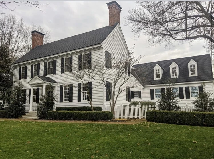A classic white house with painting exterior, black shutters, and a well-maintained lawn, featuring a small porch and attached extension.