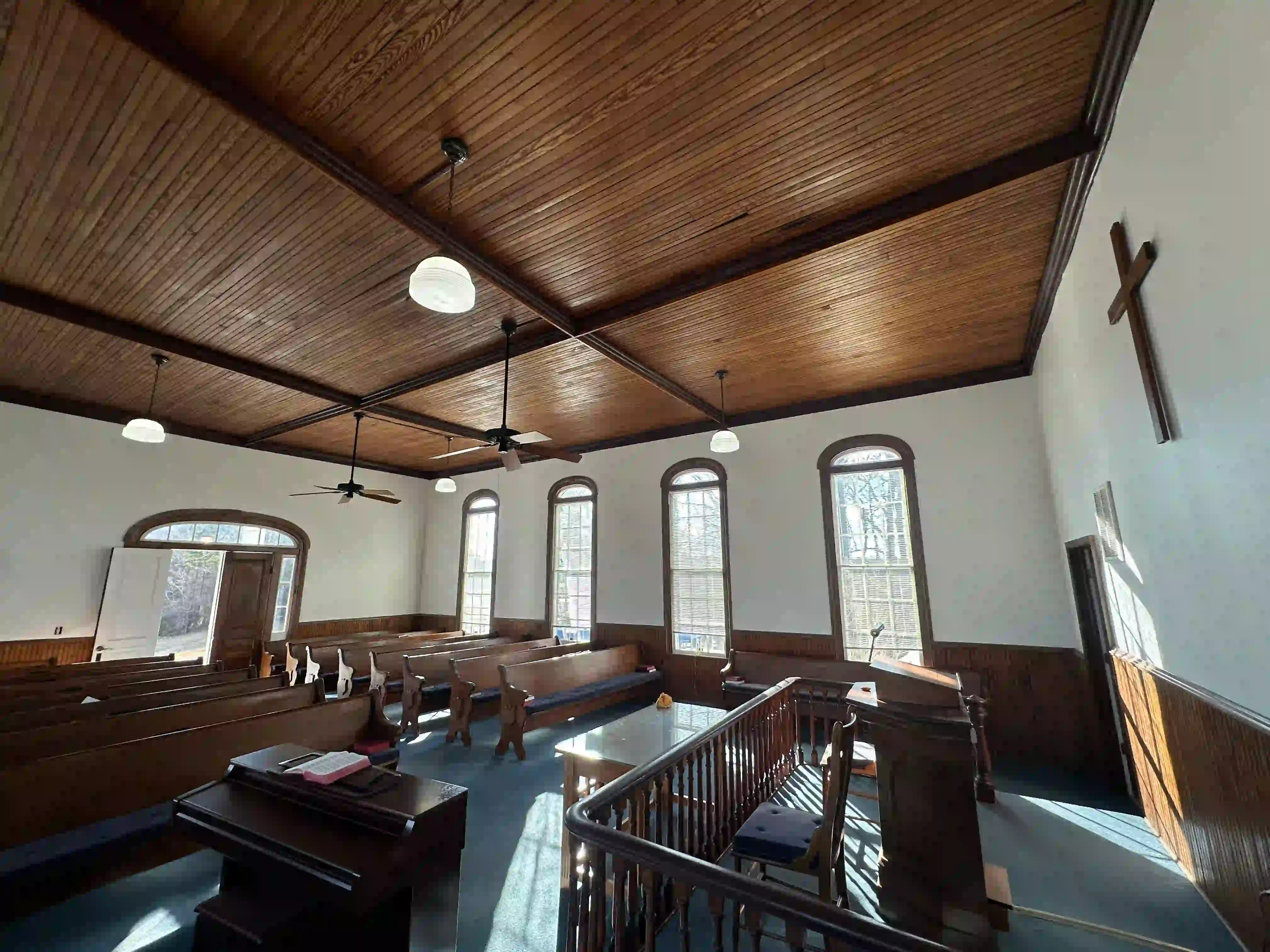 A serene church interior with wooden pews, painting ceiling, and arched windows bathed in natural light.