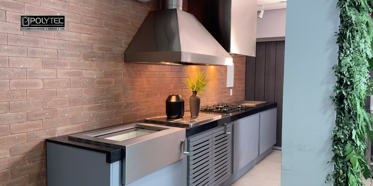 Cozinha moderna com coifa de parede inox Polytec instalada sobre cooktop, destacando ambiente elegante com parede de tijolos e ilha gourmet.