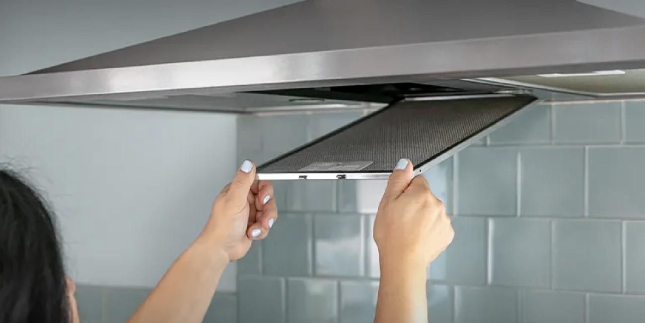 Pessoa mostrando como limpar a coifa de parede inox, removendo o filtro para higienização correta